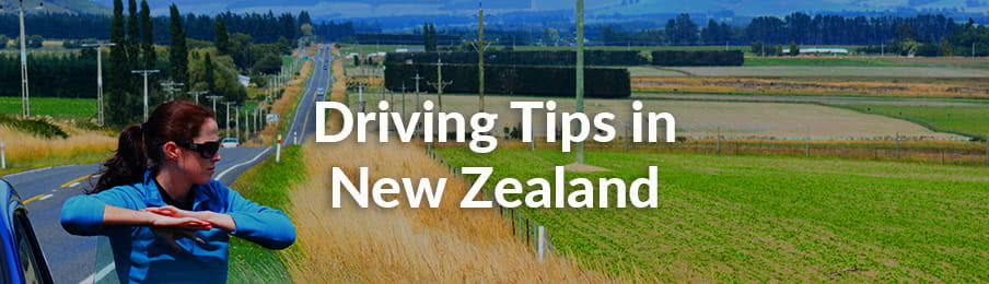 Young woman standing on the road near opened door of her rental car during travel in New Zealand.